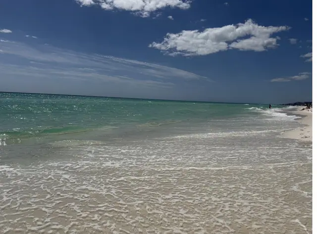 Turquoise Gulf surf washing over the white sand beach at Seaside under a blue sky.